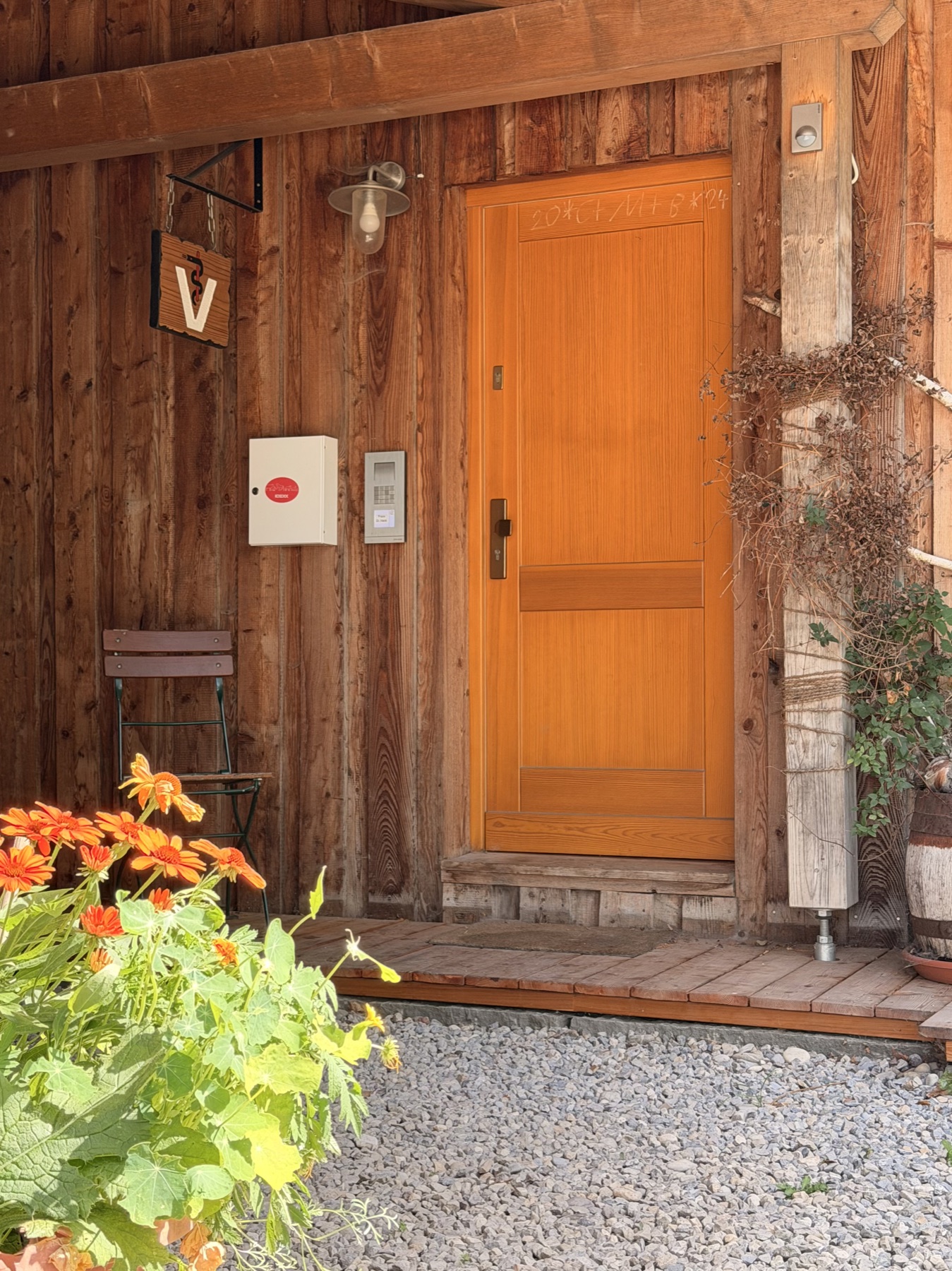 Eingang der Tierarztpraxis Steingaden: helle Holztür im Holzhaus, davor blühende Blumen